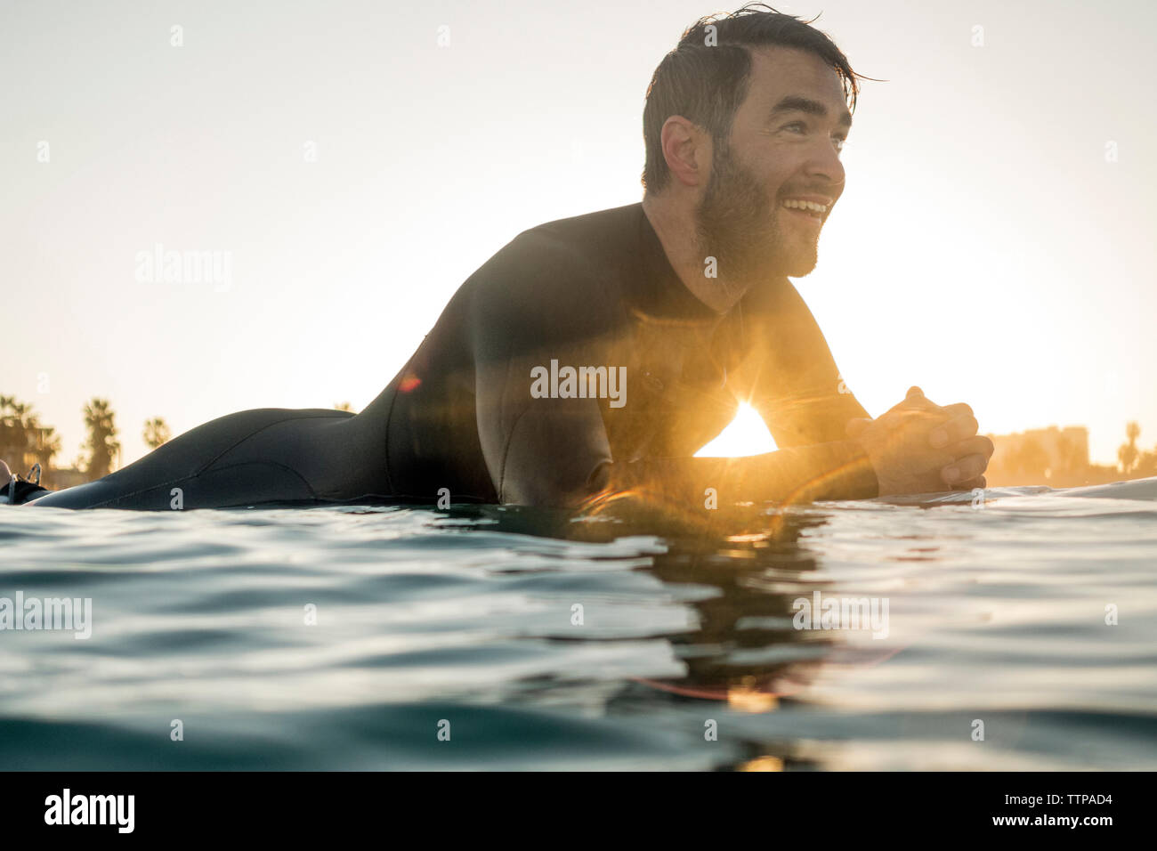 Happy male surfer lying on surfboard in sea during sunset Stock Photo