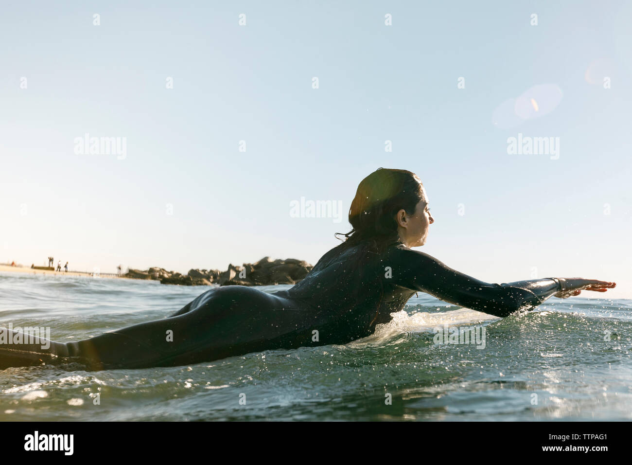 Side view of female surfer lying on surfboard in sea against clear sky