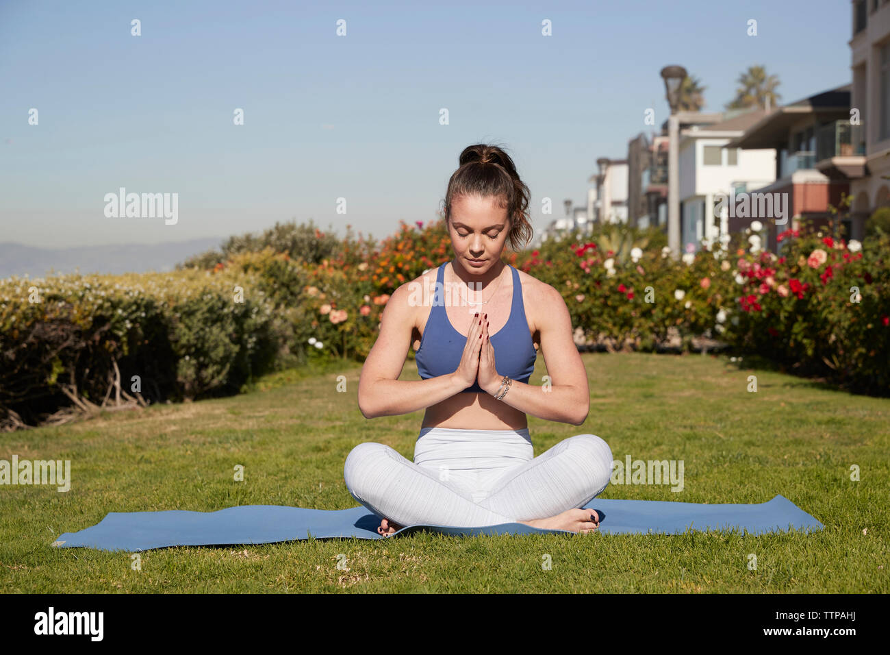 Woman with hands clasped and cross-legged meditating on exercise mat Stock Photo