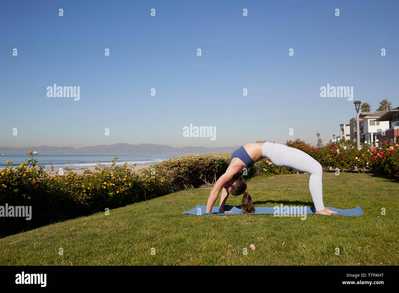 Full length of woman bending over backwards on exercise mat against clear sky Stock Photo