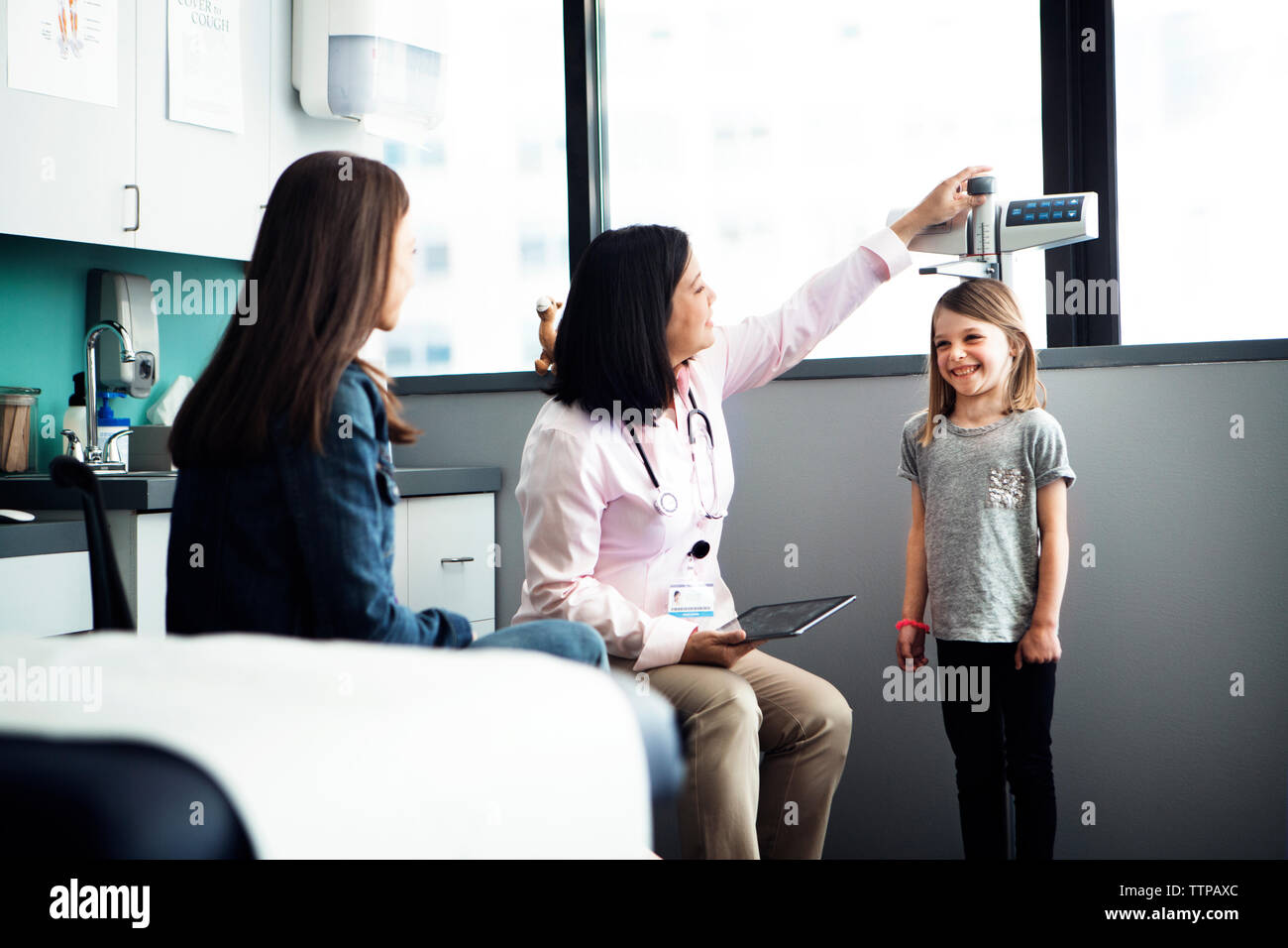Female doctor measuring girl's height while mother sitting at clinic Stock Photo