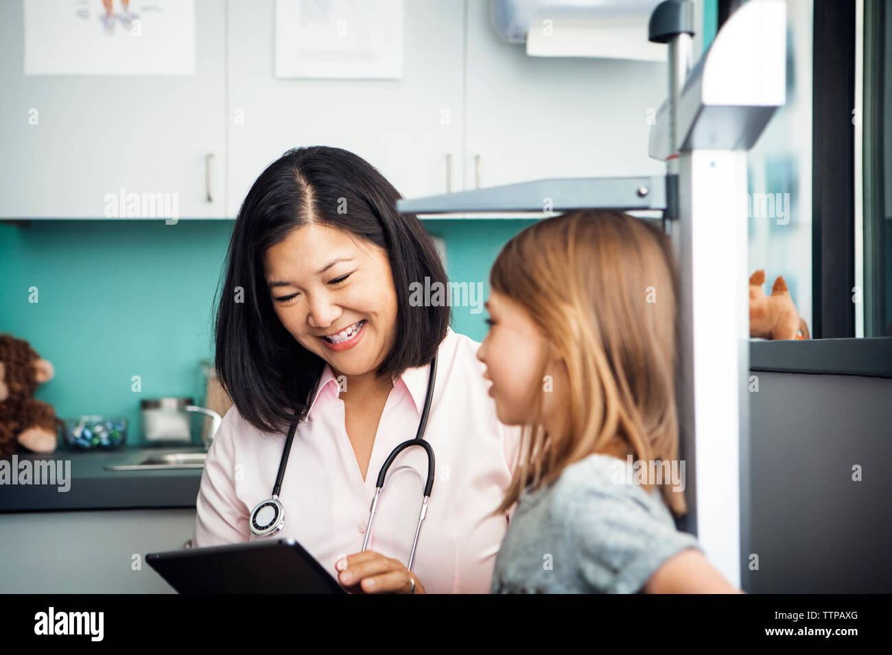 Happy female doctor using tablet computer while measuring girl's height in clinic Stock Photo