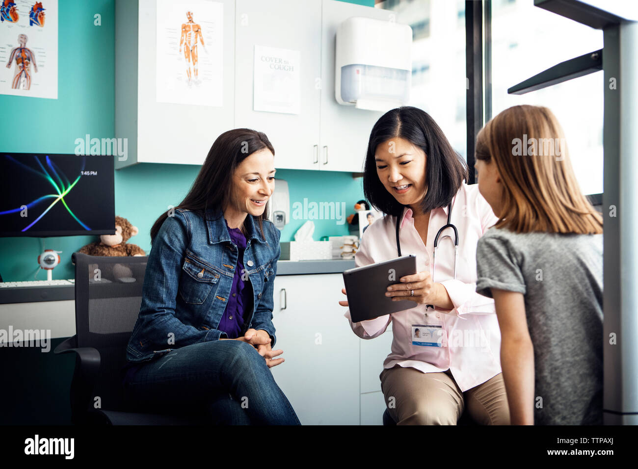 Happy female doctor showing tablet computer to family in clinic Stock Photo