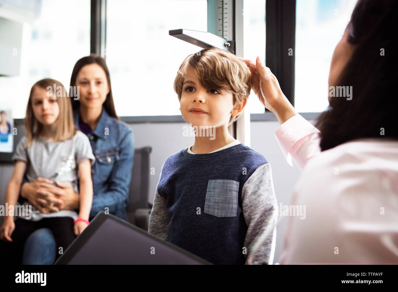 Doctor measuring boy's height while family sitting in clinic Stock Photo