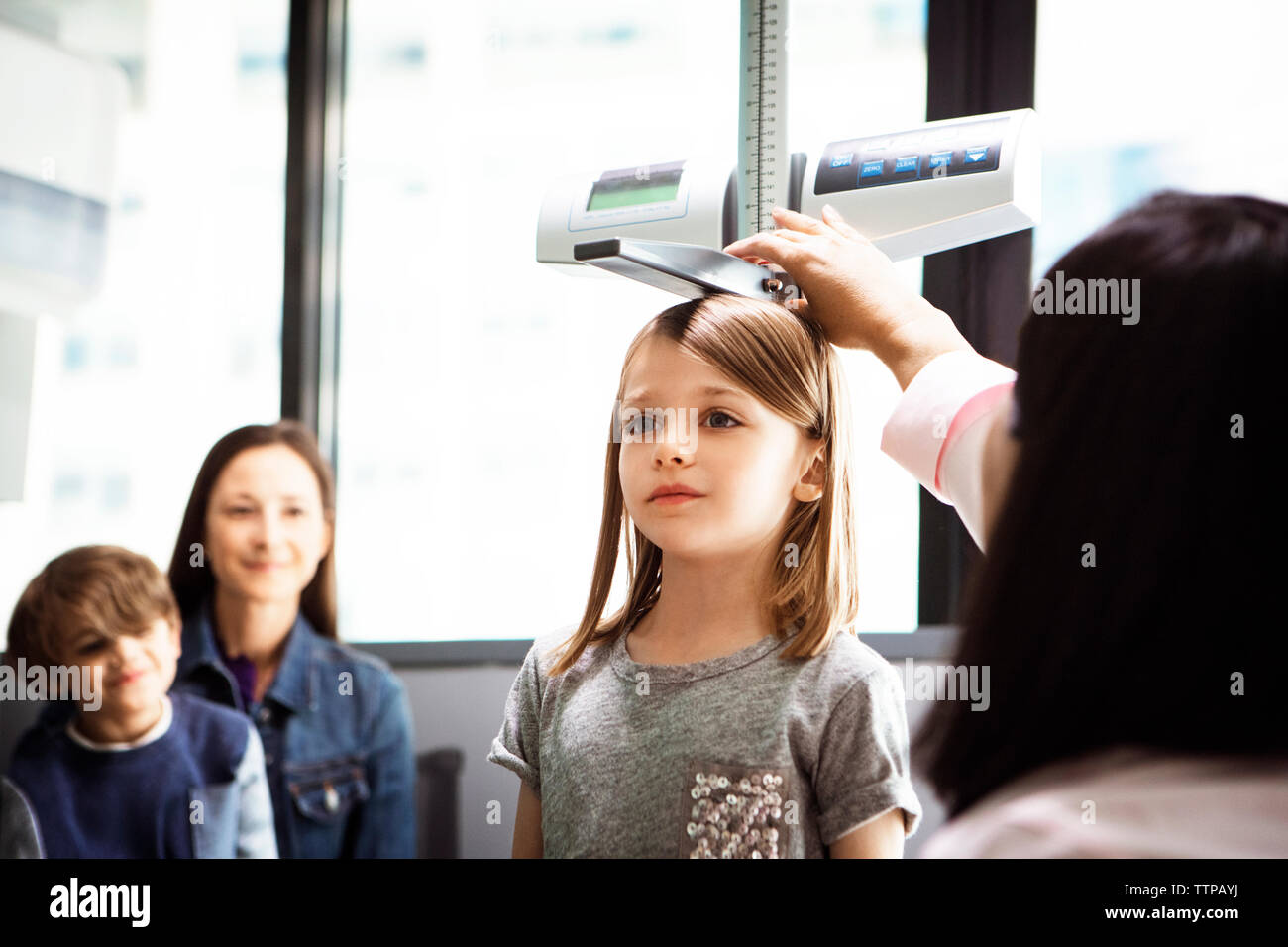 Doctor measuring girl's height while family sitting in clinic Stock Photo
