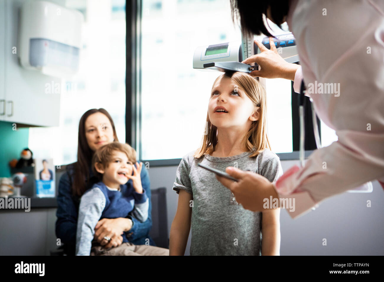 Doctor measuring girl's height while family sitting at clinic Stock Photo