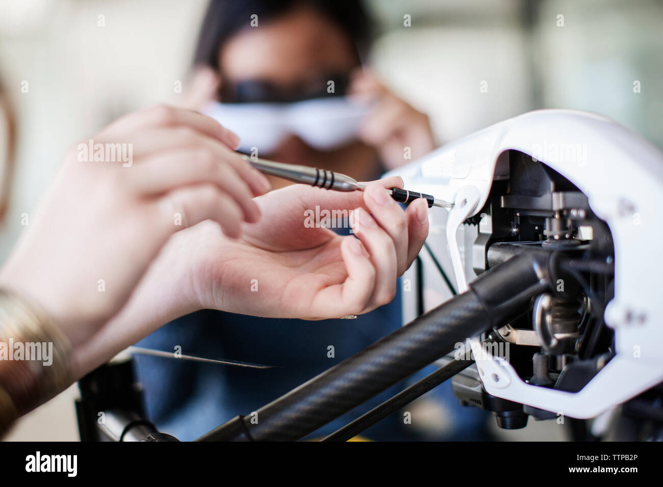 Cropped image of female student working on drone with friend in background Stock Photo