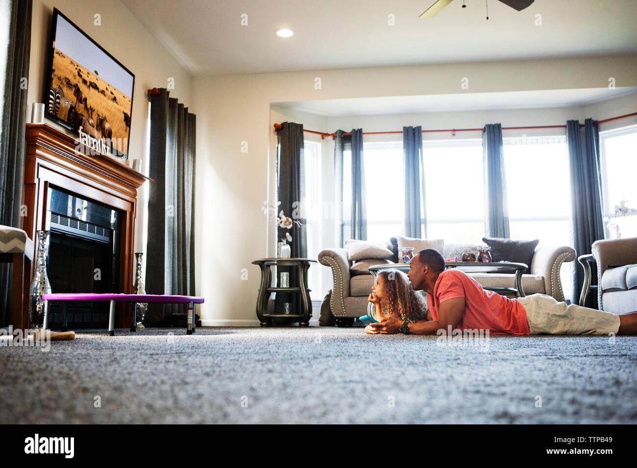 Father and daughter watching TV while lying on carpet at home Stock Photo