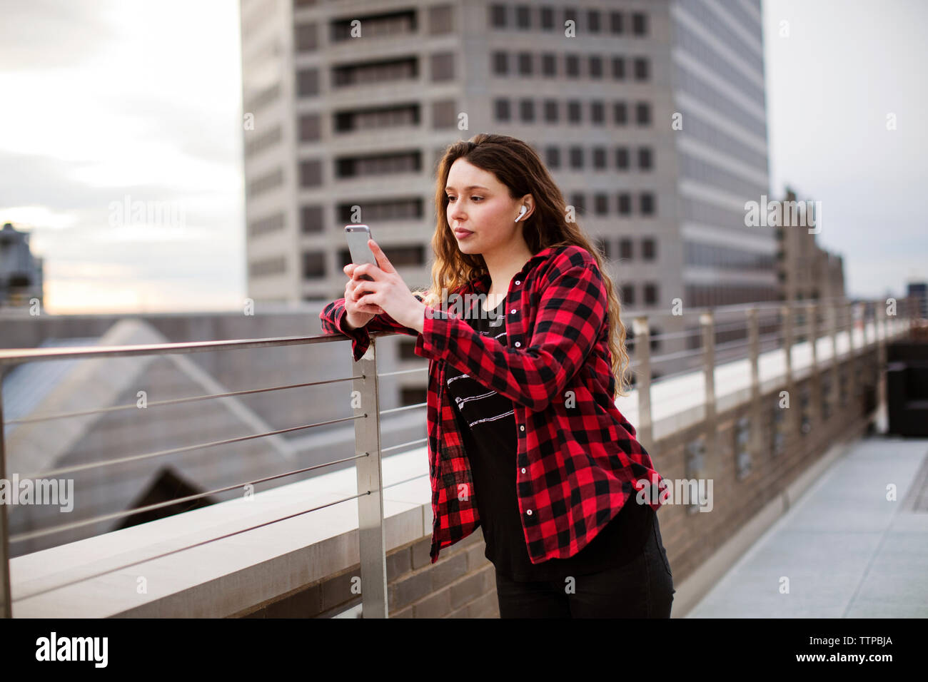 Young female using smart phone while standing by railing at terrace Stock Photo