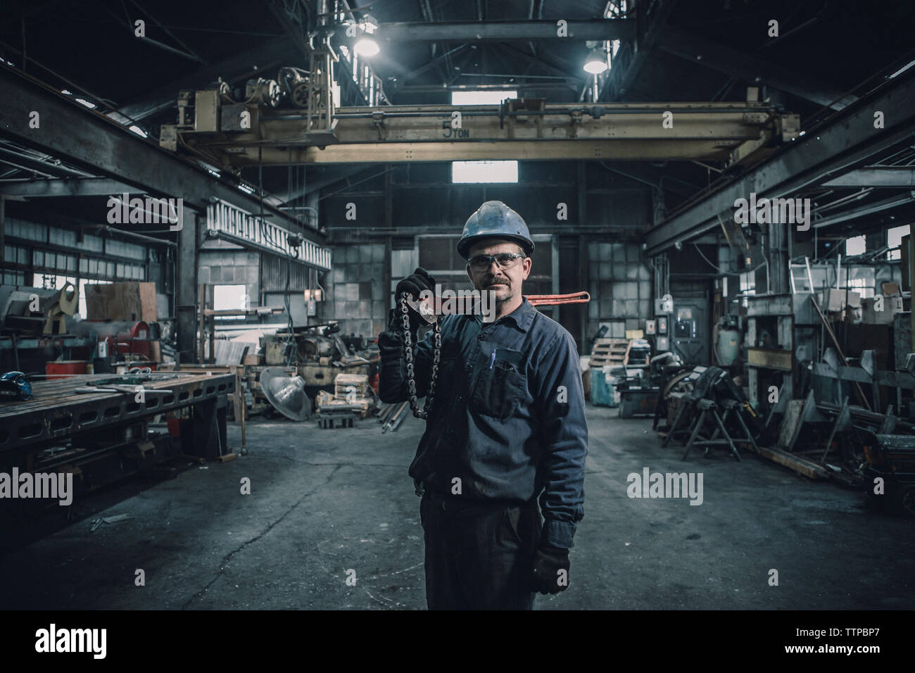 Portrait of male worker carrying work tool while standing in factory Stock Photo