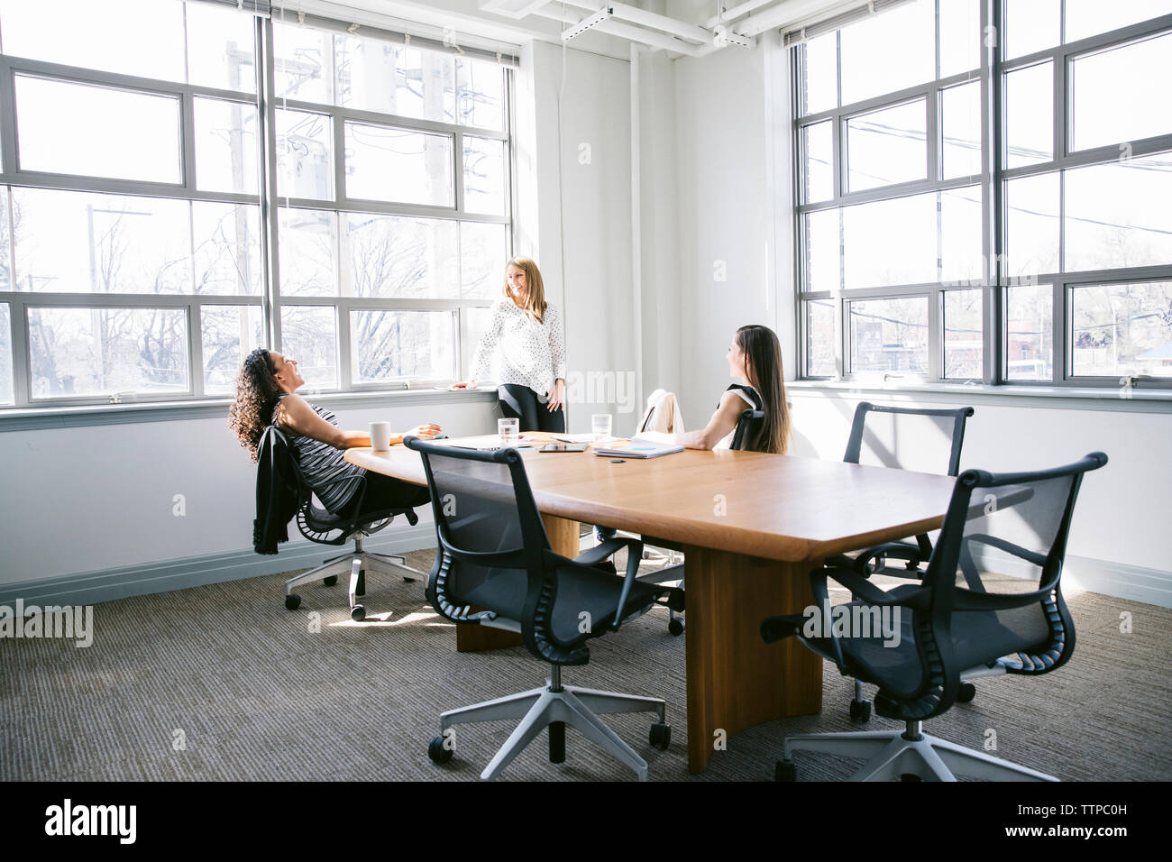 Cheerful female colleagues talking in board room Stock Photo