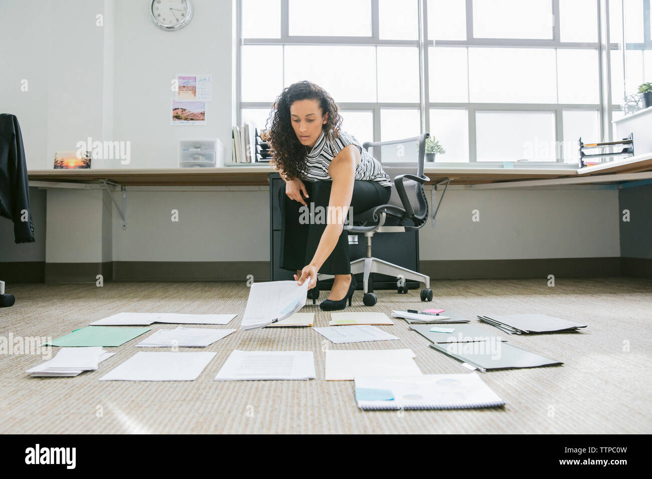 businesswoman arranging documents on floor in office Stock Photo