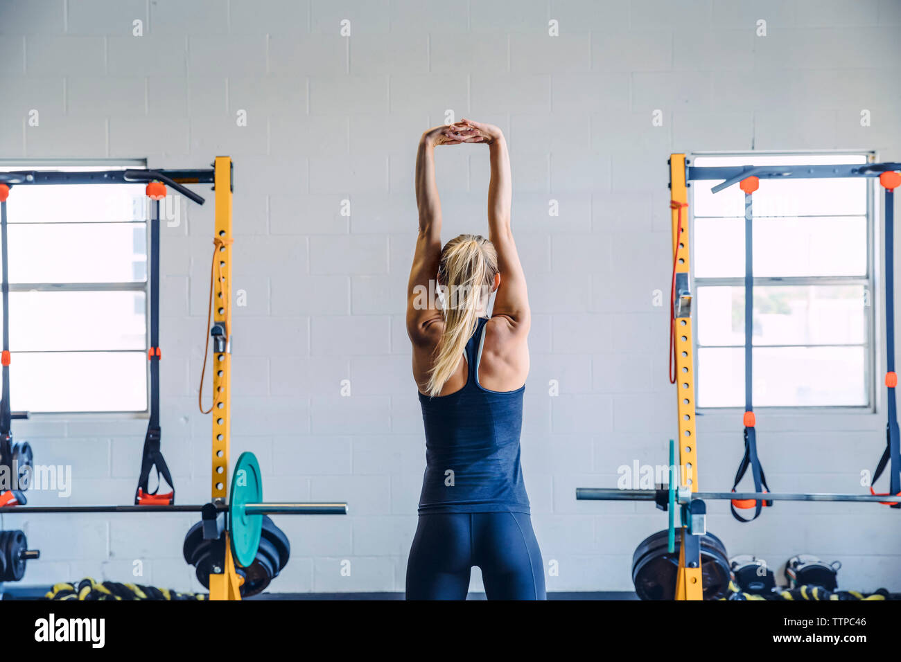 Rear view of woman with hands clasped exercising against wall in gym Stock Photo