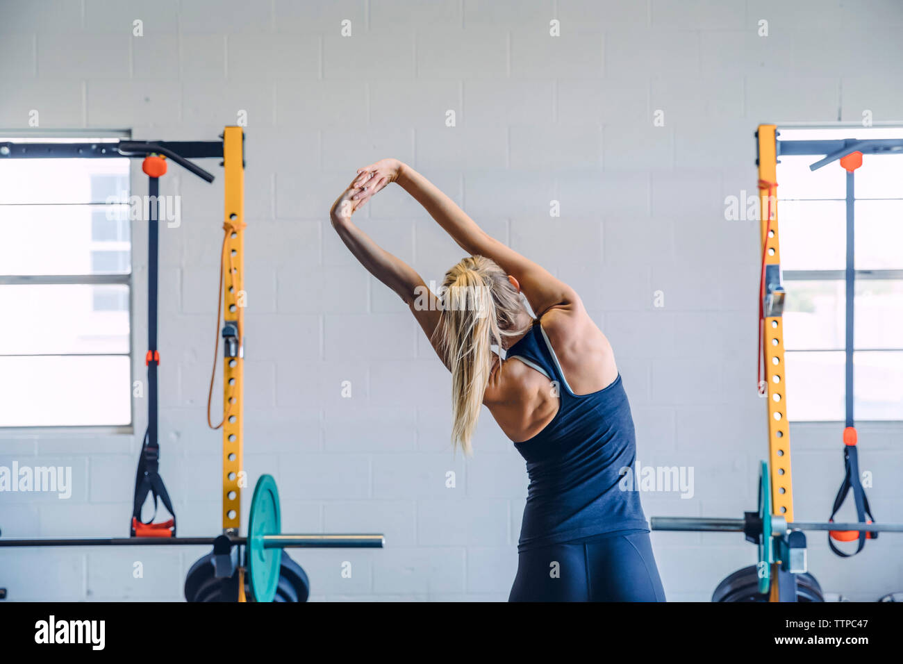 Rear view of woman with hands clasped stretching while exercising against wall in gym Stock Photo