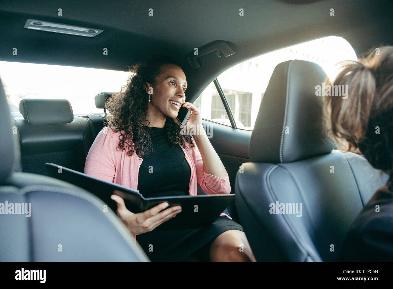 businesswoman talking on smart phone while holding file in car Stock Photo