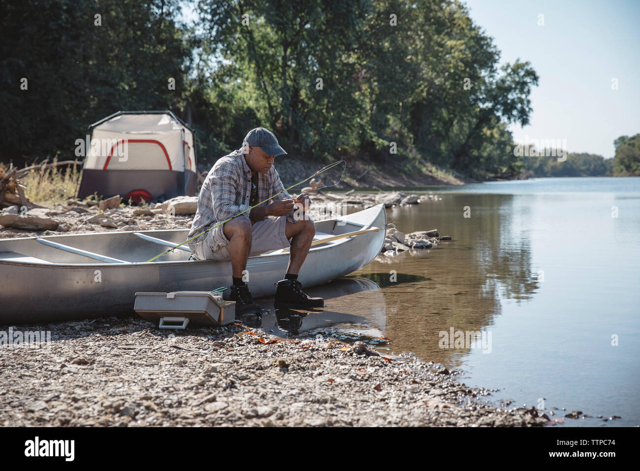 Man adjusting fishing tackle while sitting on boat at lakeshore Stock Photo