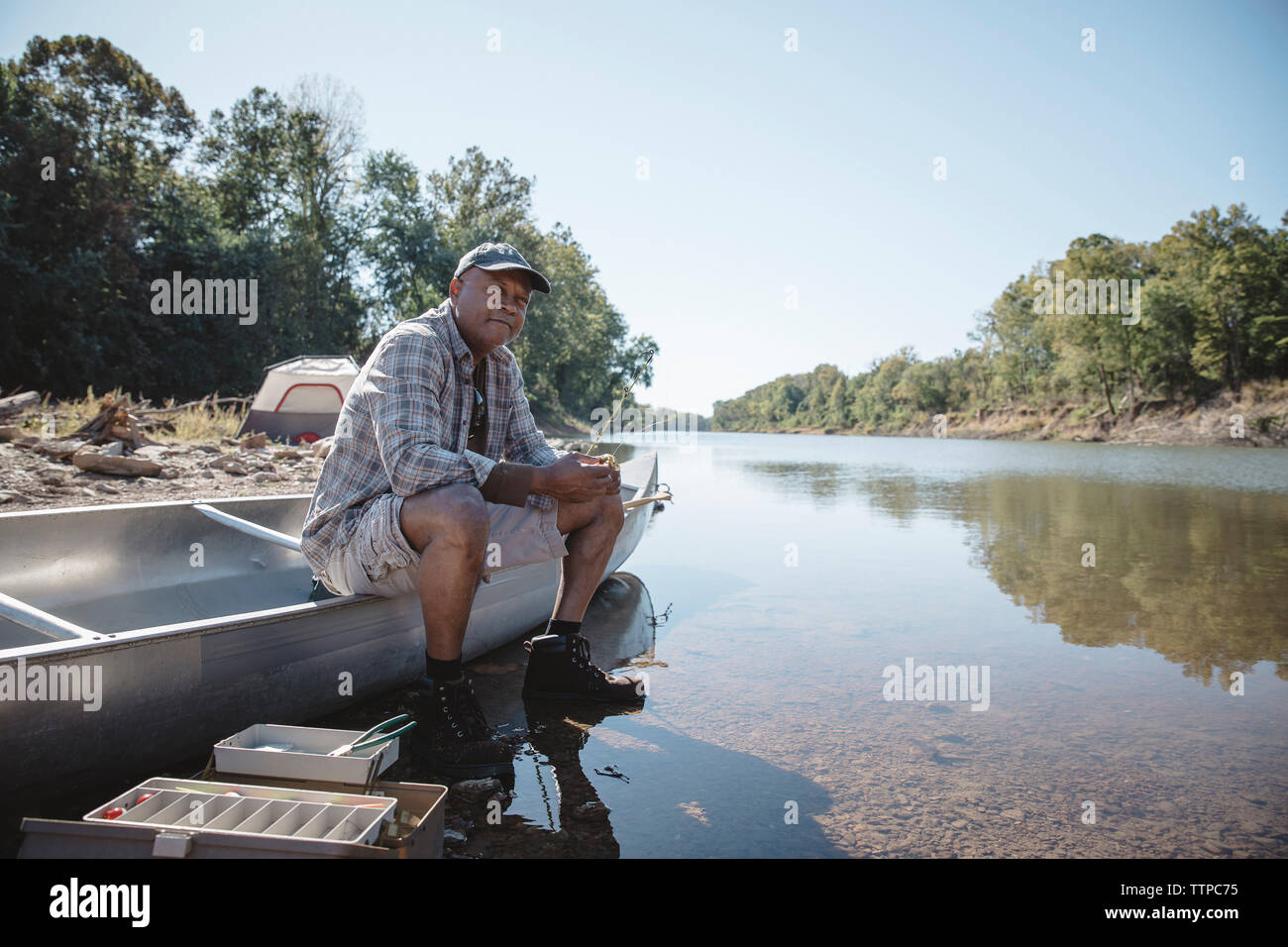 Man holding fishing rod while sitting on boat at lakeshore Stock Photo