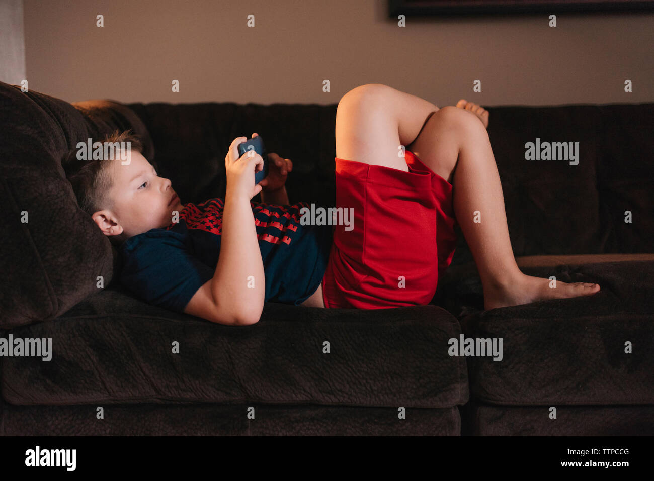Boy using mobile phone while lying on sofa at home Stock Photo