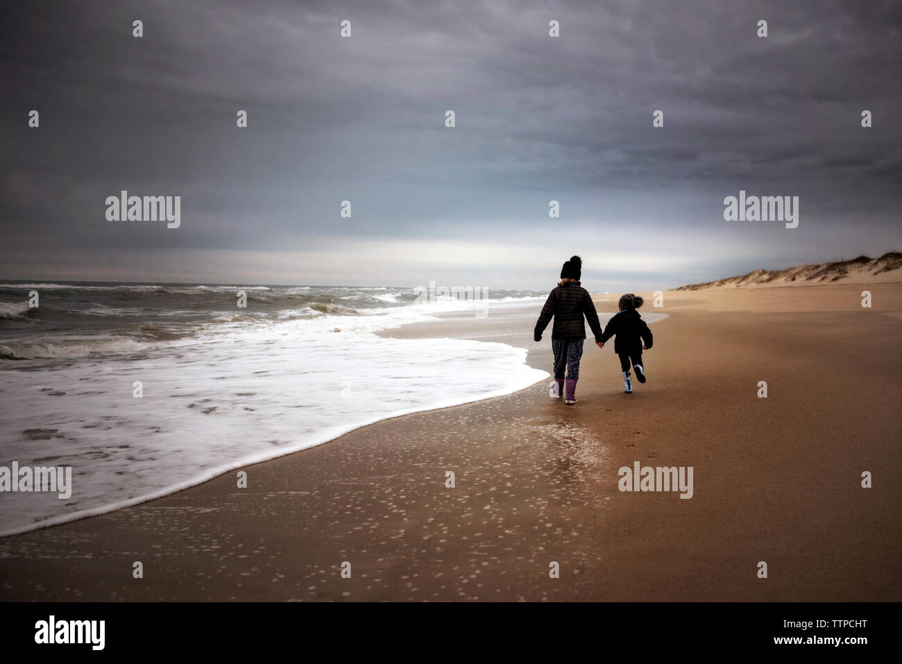 Young girls holding hands running down the beach against cloudy sky Stock Photo