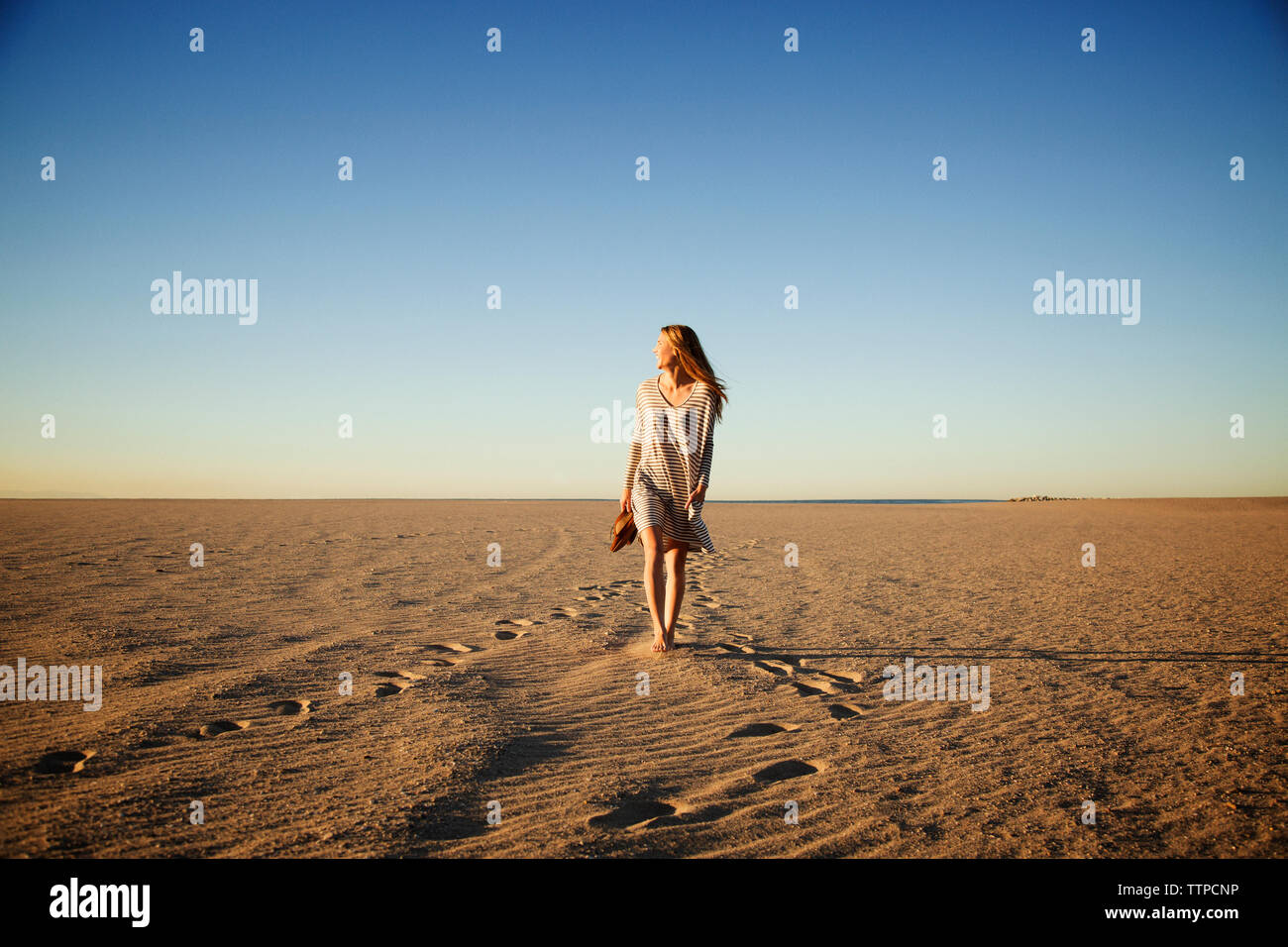 Carefree woman walking on beach against clear blue sky during sunset Stock Photo