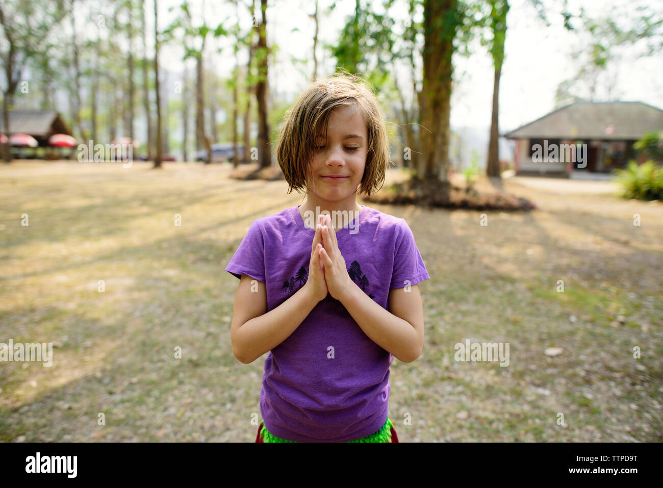 Girl with eyes closed doing hands clasped while standing against sky Stock Photo