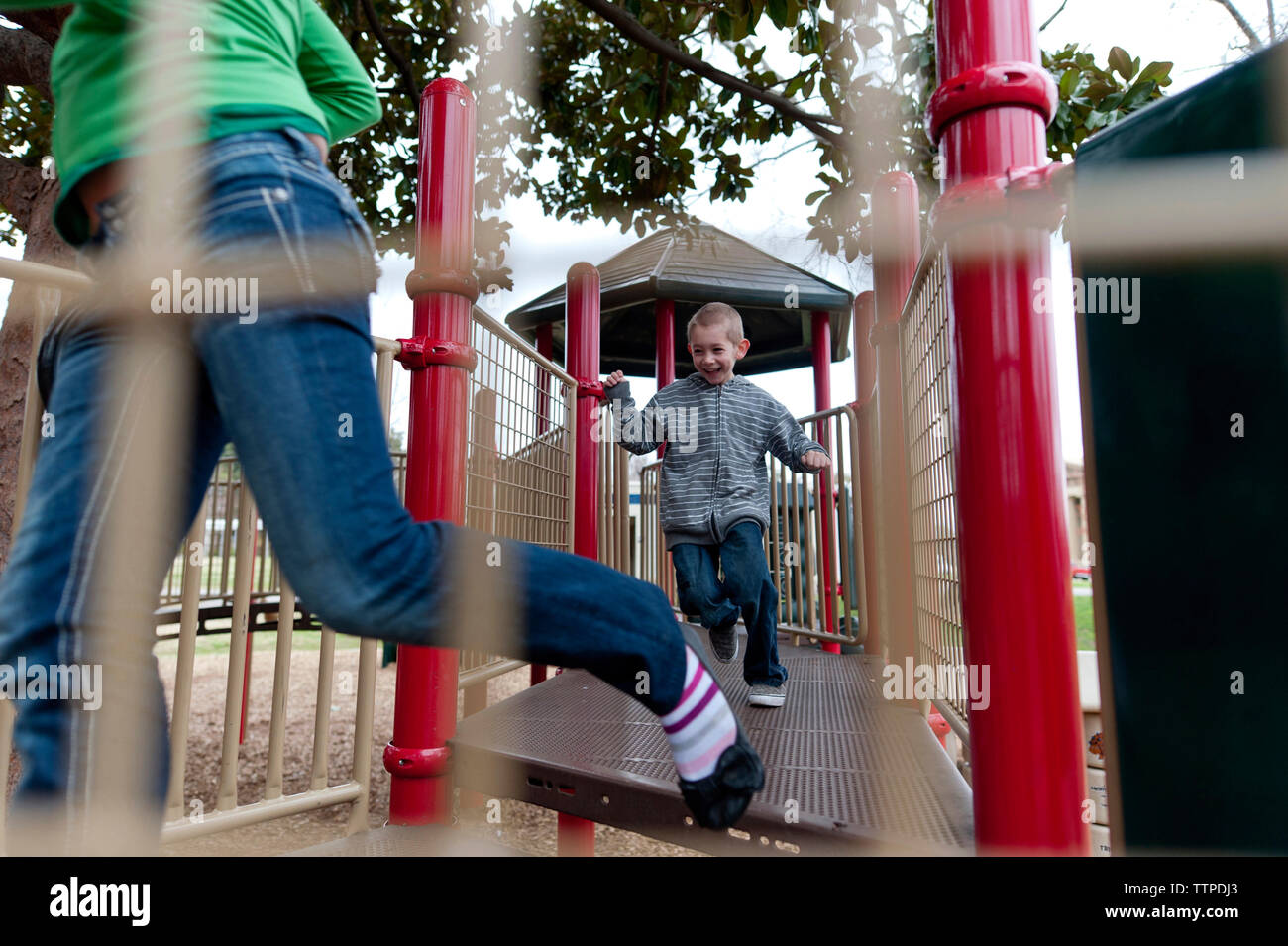 Siblings running on outdoor play equipment at playground Stock Photo