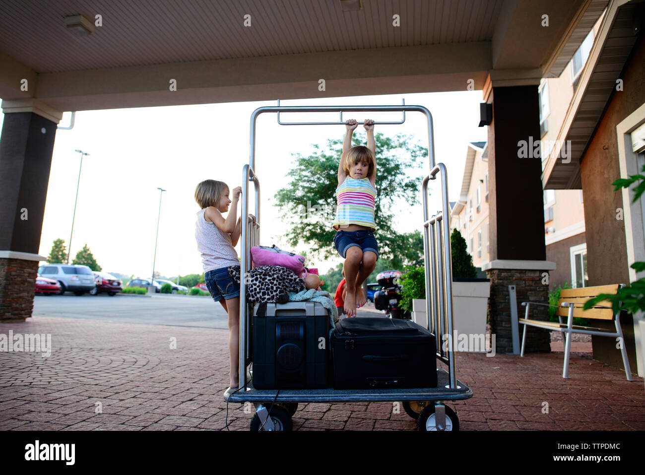Sisters playing on luggage cart outside hotel Stock Photo Alamy