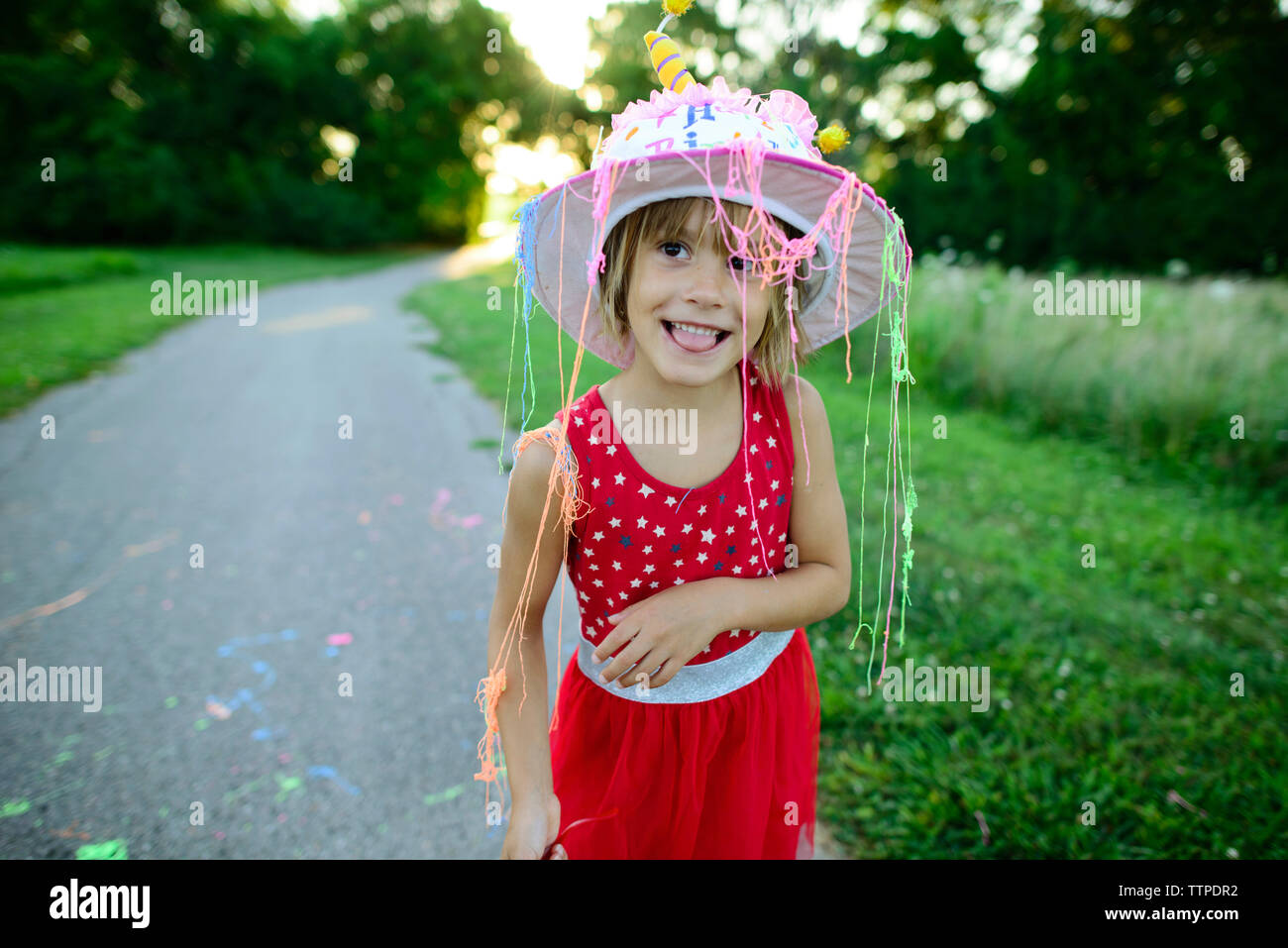 Girl in birthday cake hat looking away while sticking out tongue on road Stock Photo