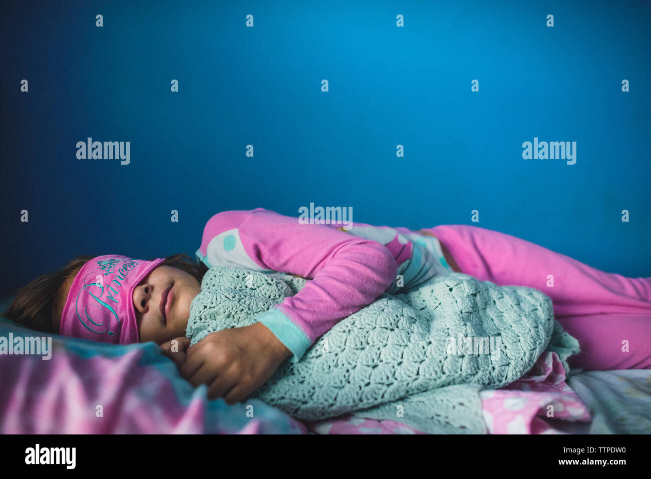 Girl wearing eye mask while sleeping on bed against wall Stock Photo