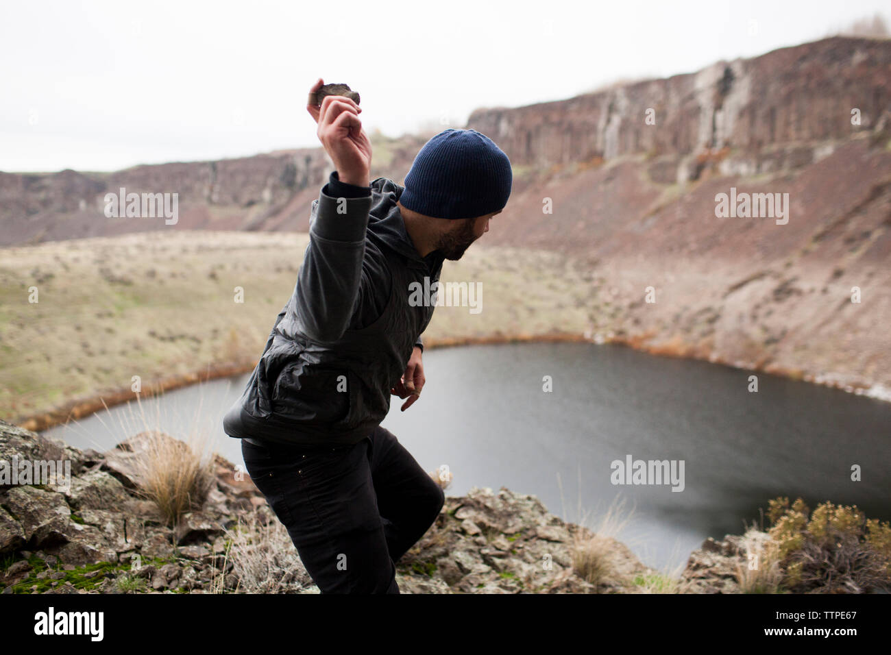 Side view of hiker throwing stone in lake while standing on cliff Stock Photo