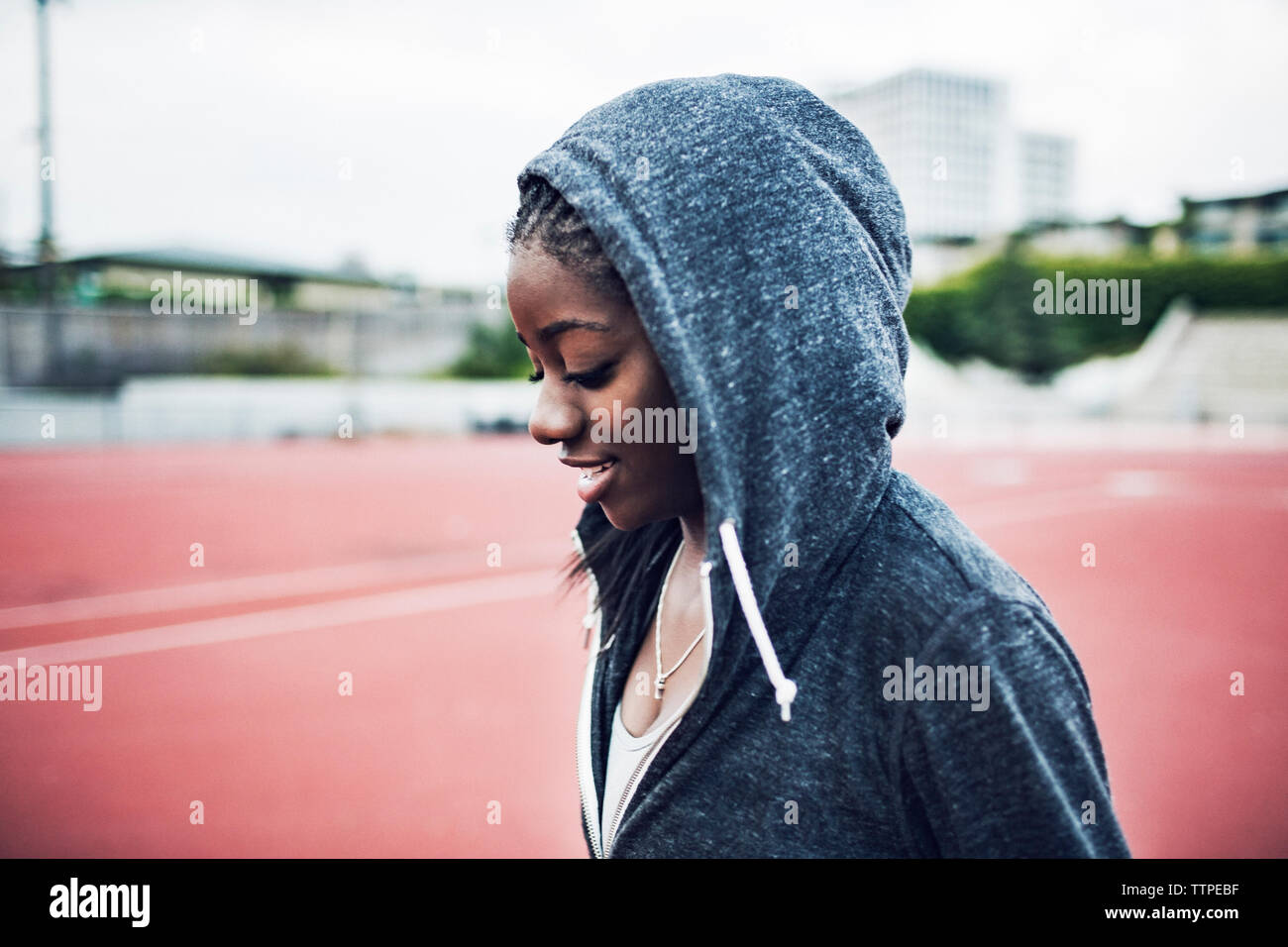 Smiling sportswoman wearing hooded jacket on running tracks Stock Photo