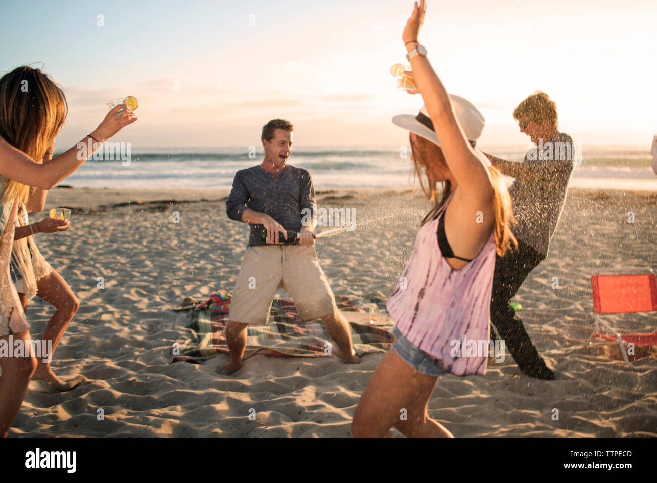 Happy man opening wine bottle while friends dancing on beach Stock Photo