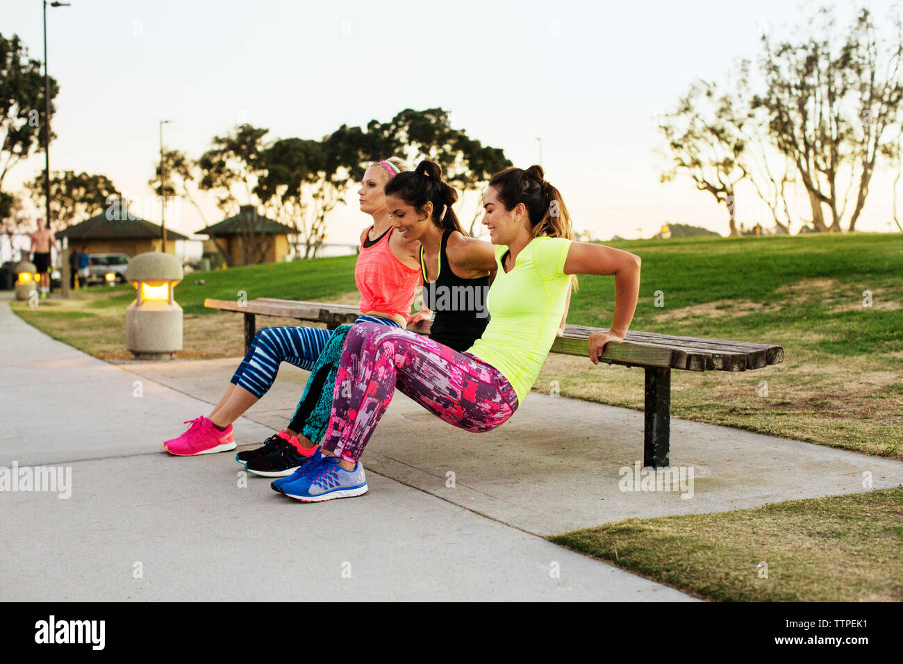 Friends doing reverse push-ups on bench at park Stock Photo