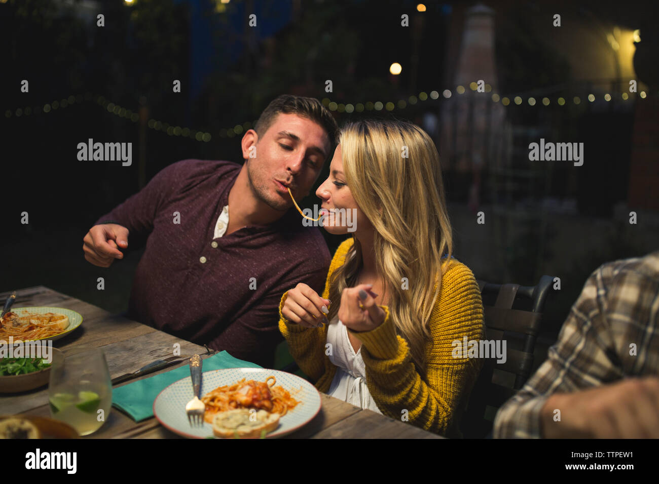 Playful couple eating pasta while enjoying dinner party with friends Stock Photo