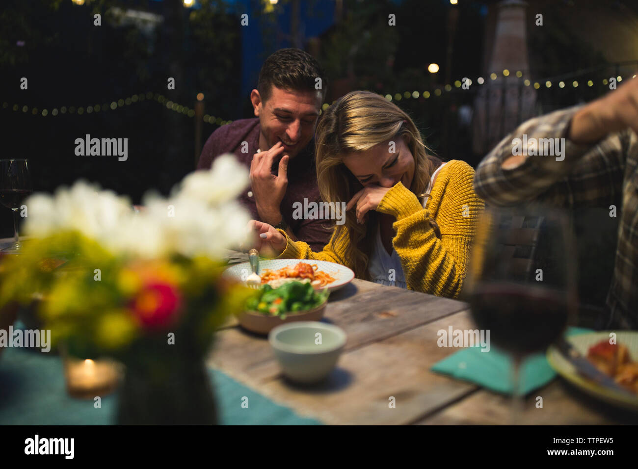 Happy couple sitting at table while enjoying dinner party with friends Stock Photo