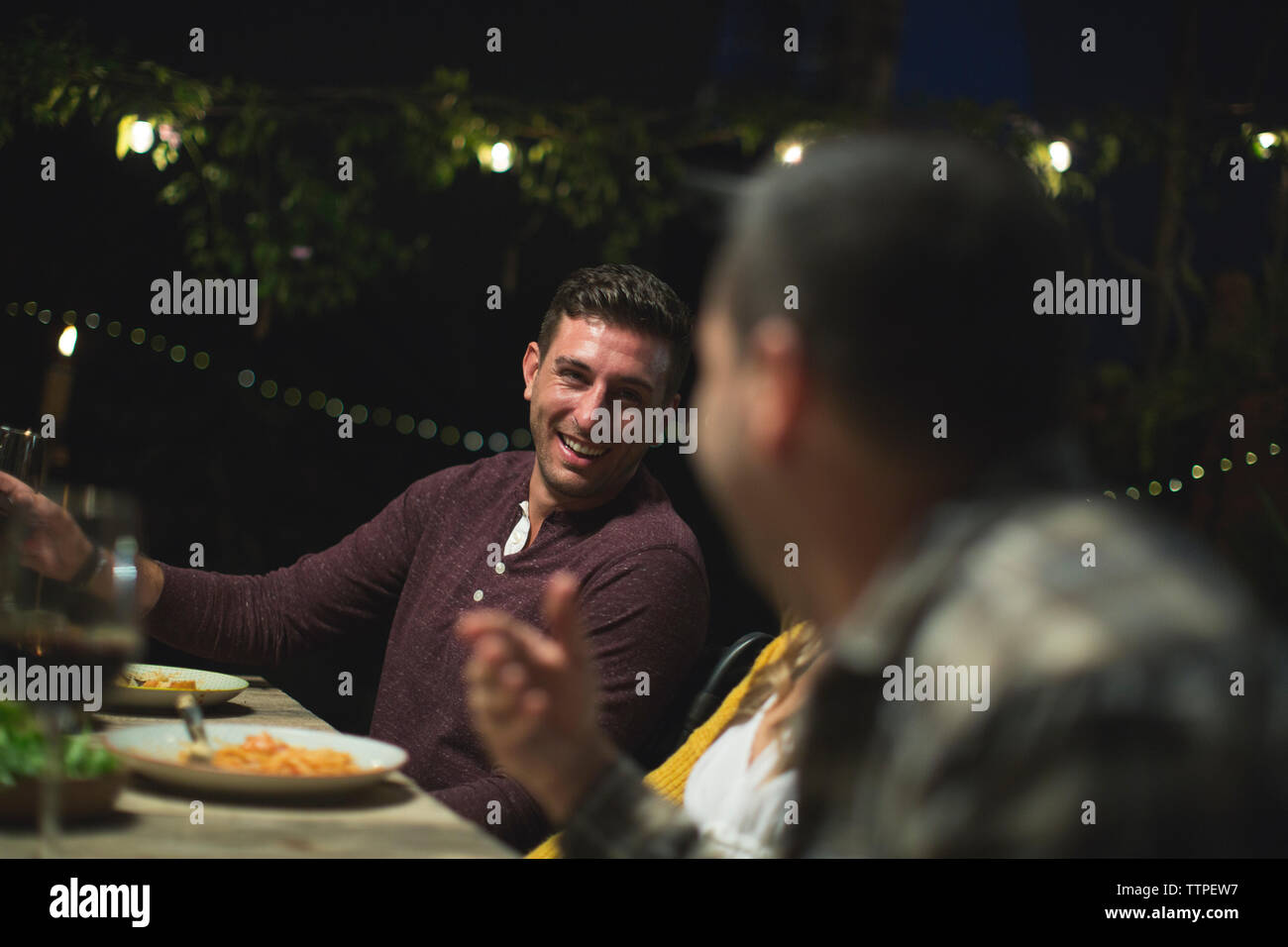 Smiling friends talking while sitting at table during dinner party Stock Photo