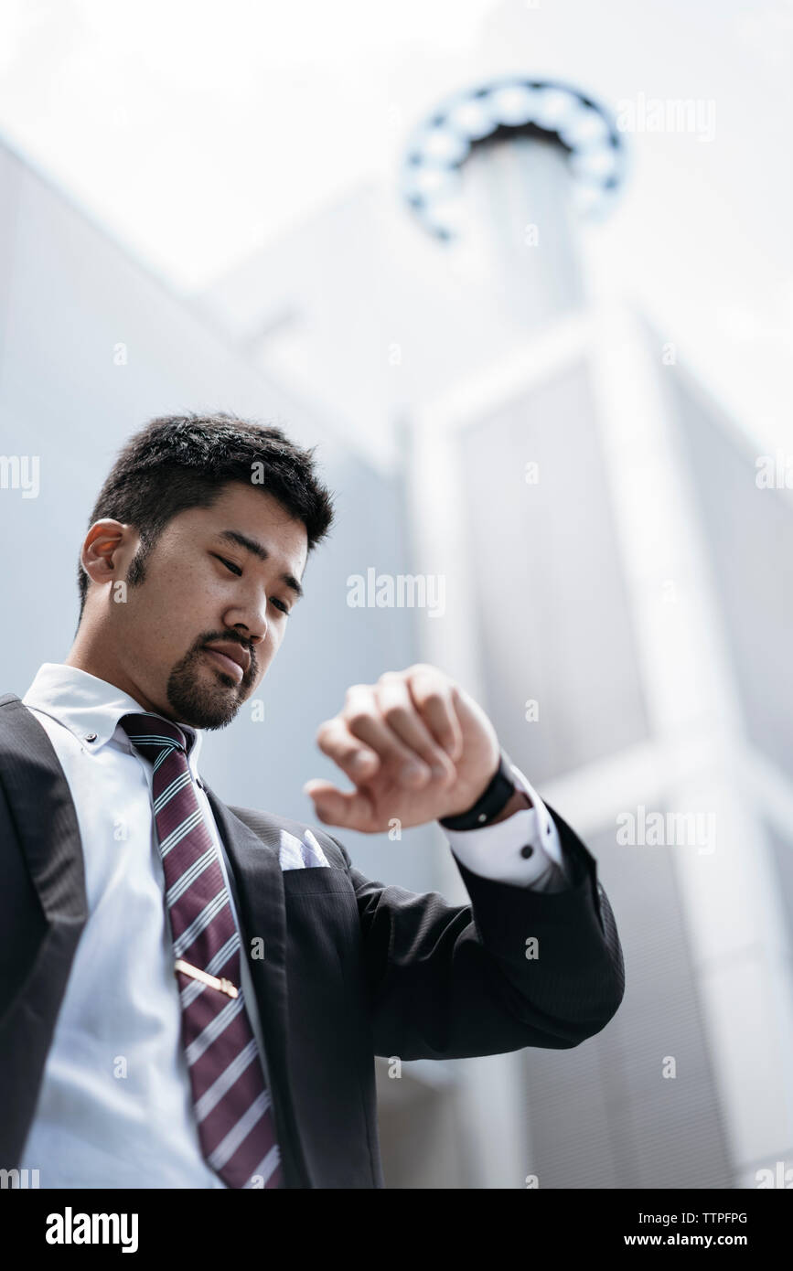 Low angle view of businessman checking time on smart watch outside office building Stock Photo