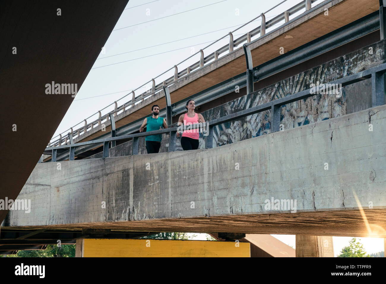 Low angle view of young couple jogging together on bridge Stock Photo