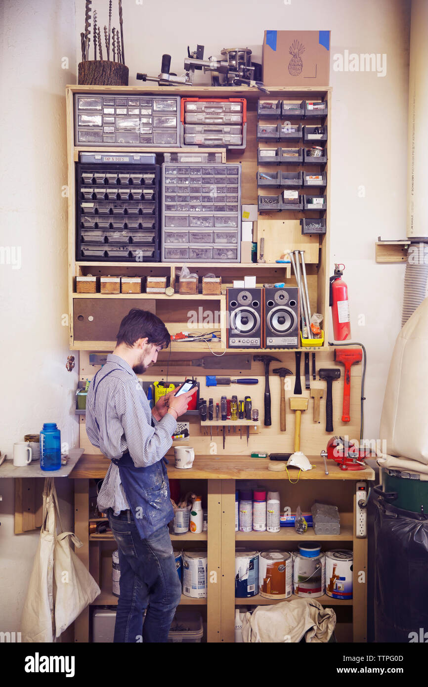 Craftsperson using phone while standing by tools at workshop Stock Photo