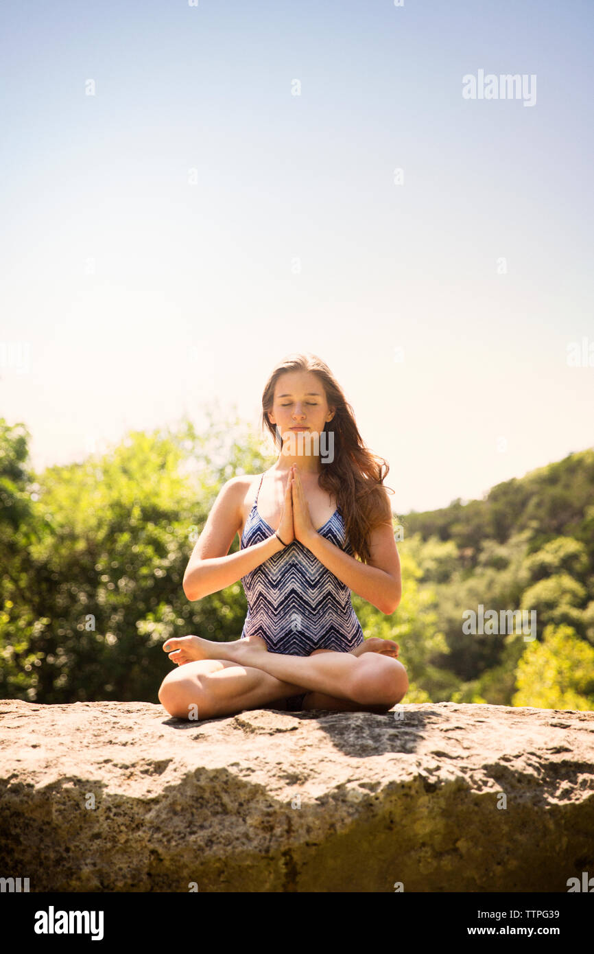 Teenager meditating on top of rock against clear sky at forest Stock Photo