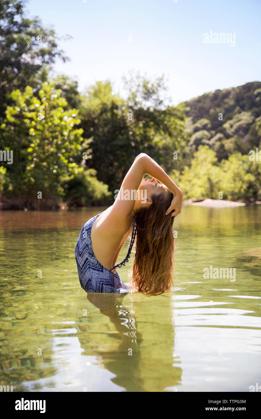 Side view of teenager standing in lake with head up at forest Stock Photo