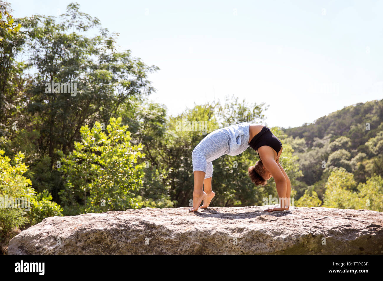 Woman doing bridge pose on rock against clear sky at forest Stock Photo