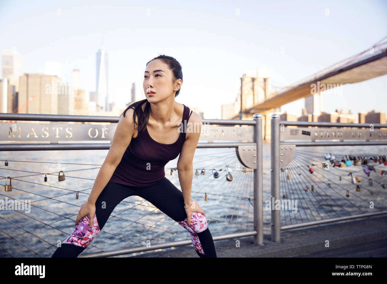 Thoughtful female athlete exercising on promenade with Brooklyn Bridge and One World Trade Center in background Stock Photo