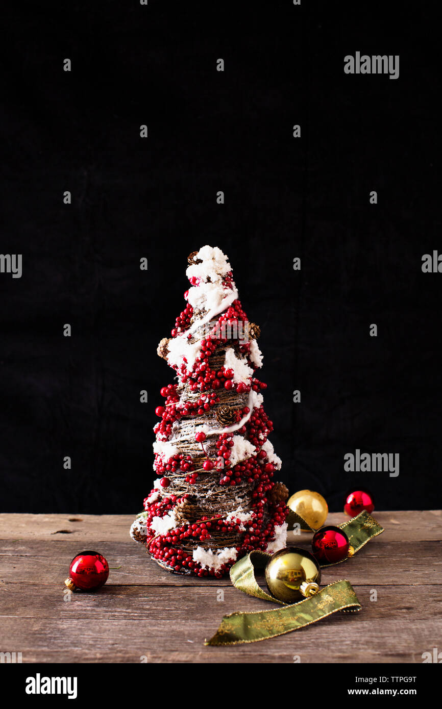 Close-up of artificial christmas tree with baubles on wooden table against black background Stock Photo