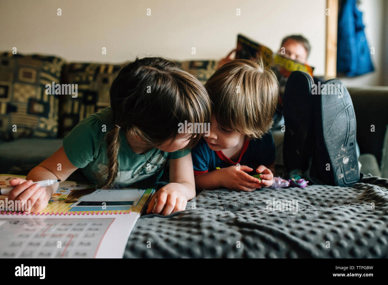 Siblings drawing while lying by father on bed at home Stock Photo