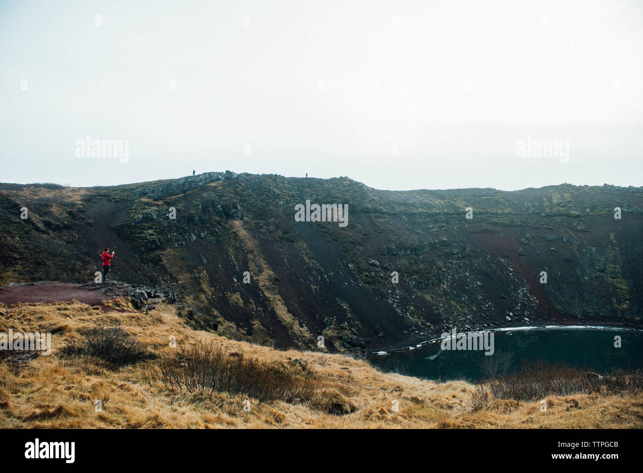 Man In Red Standing At The Edge Of A Lake Filled Crater in Iceland Stock Photo