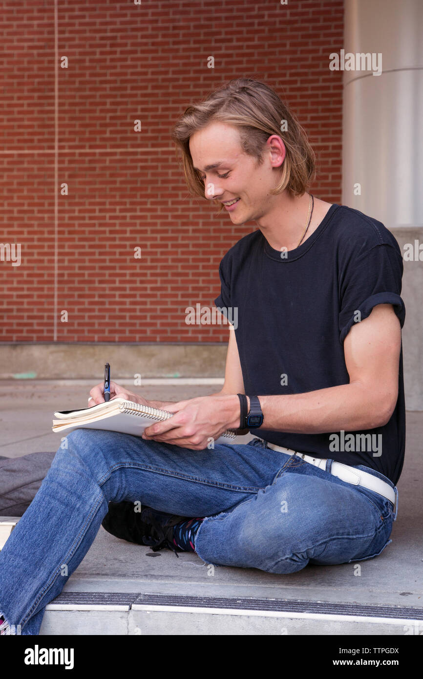 Male student smiling and writing on notebook Stock Photo