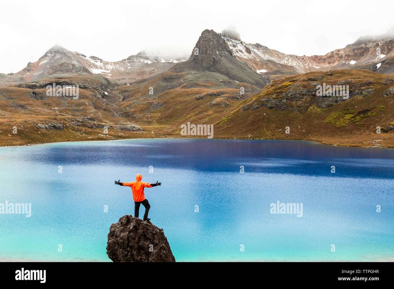Rear view of man standing on rock against lake Stock Photo
