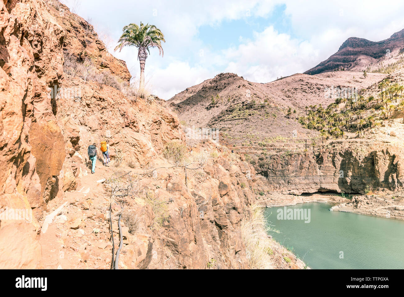 Mid distance view of female backpackers walking on rock formation by lake at desert Stock Photo