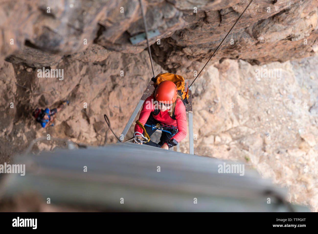 High angle view of female hiker wearing helmet while climbing on rope ladder amidst mountains Stock Photo